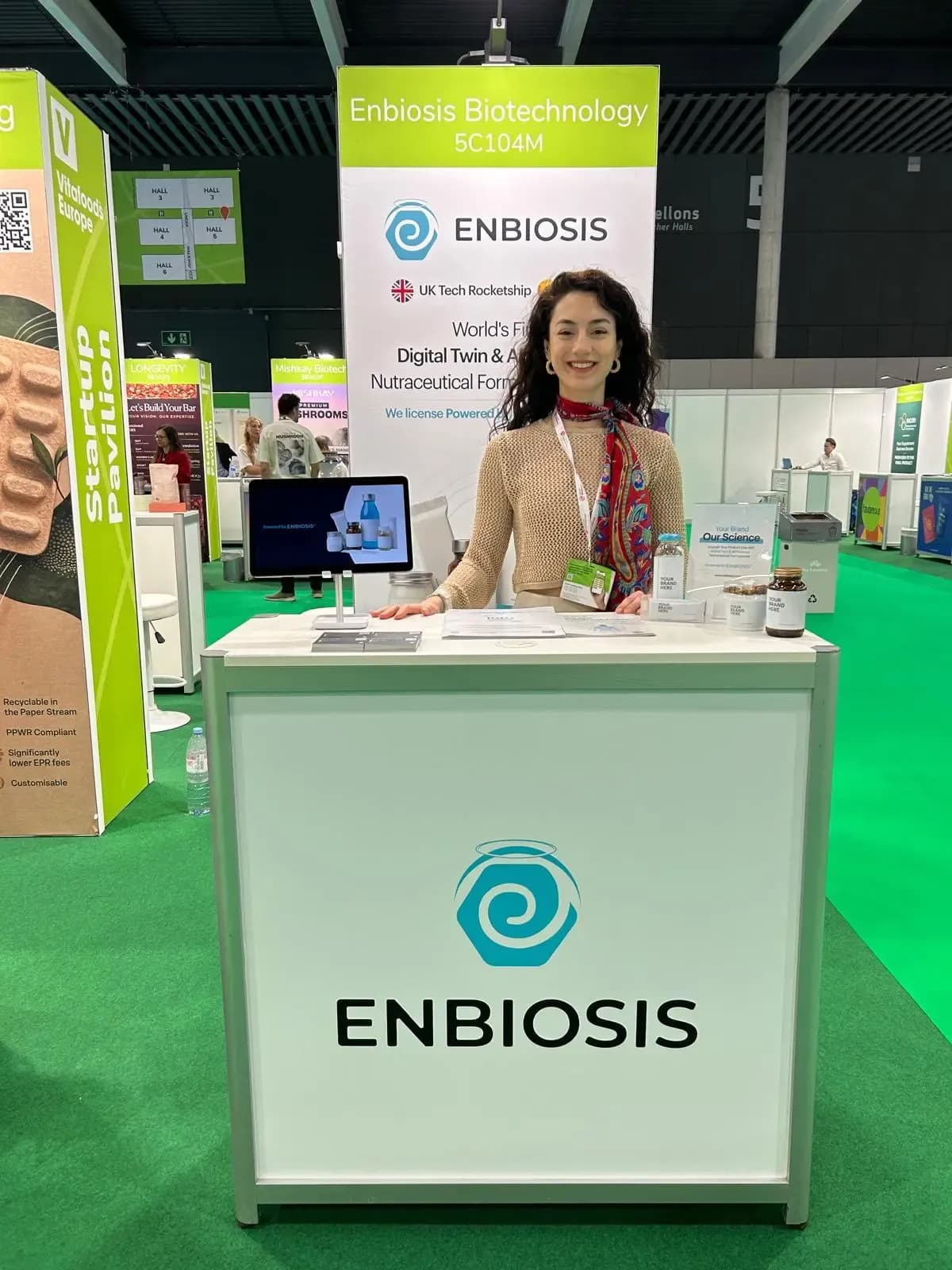 A person staffing the Enbiosis stand at Vitafoods Europe, standing behind the branded counter