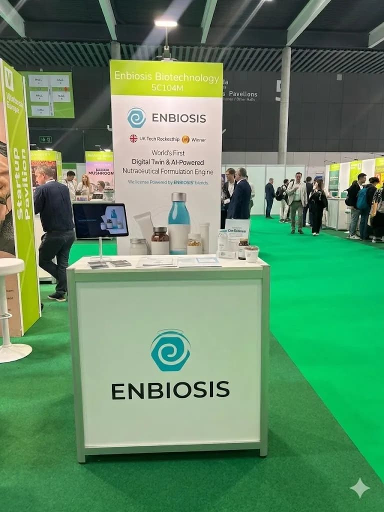 The Enbiosis stand at Vitafoods Europe, with product samples on a branded counter and a banner reading World's First Digital Twin and AI-Powered Nutraceutical Formulation Engine